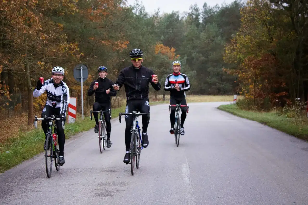 Peleton kolarzy jedzie drogą wśród jesiennych drzew. Czy to wyścig, czy wspólna przejażdżka?