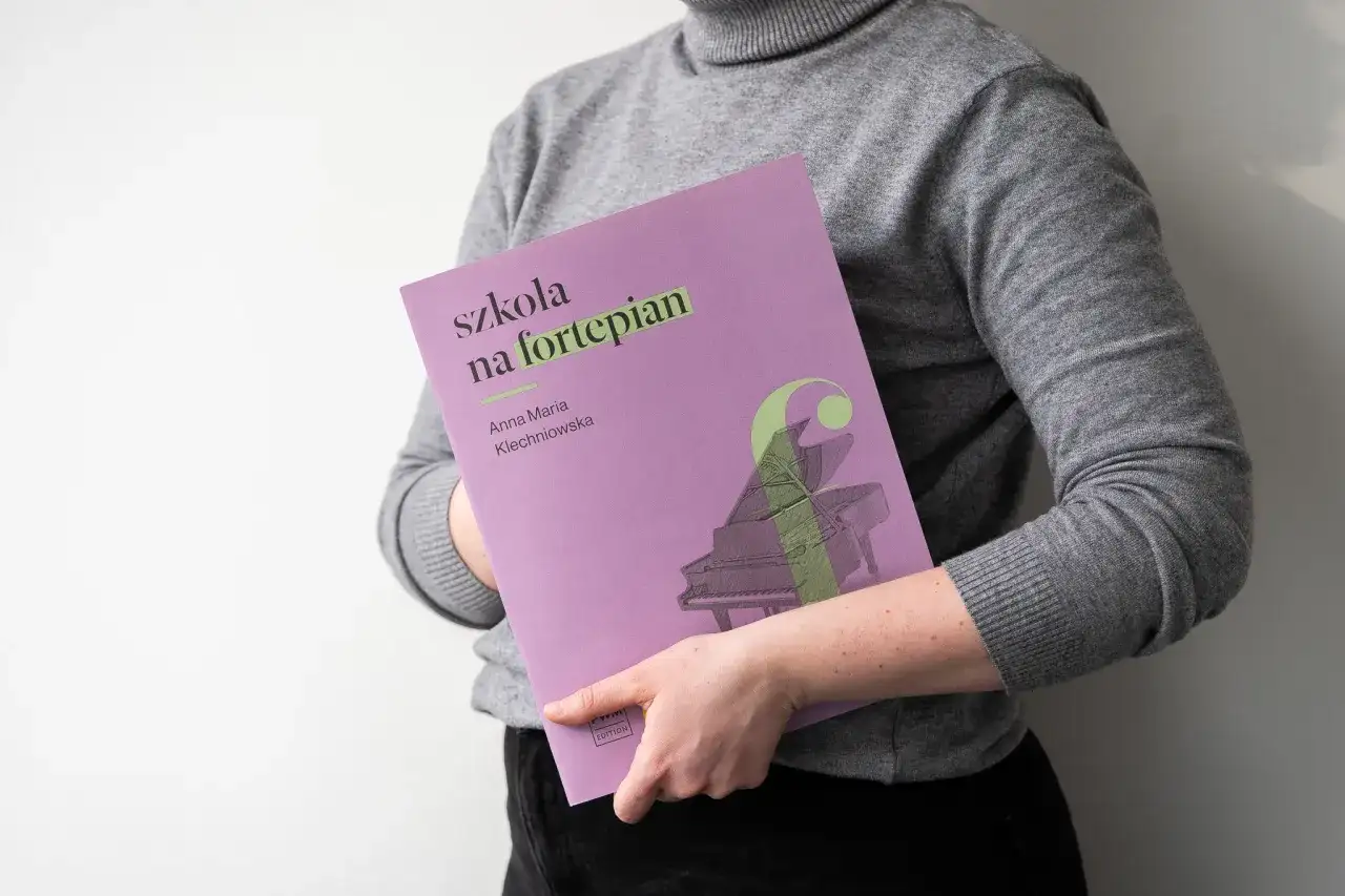 Osoba trzyma okładkę "Szkoła na fortepian Klechniowska" z grafiką fortepianu.