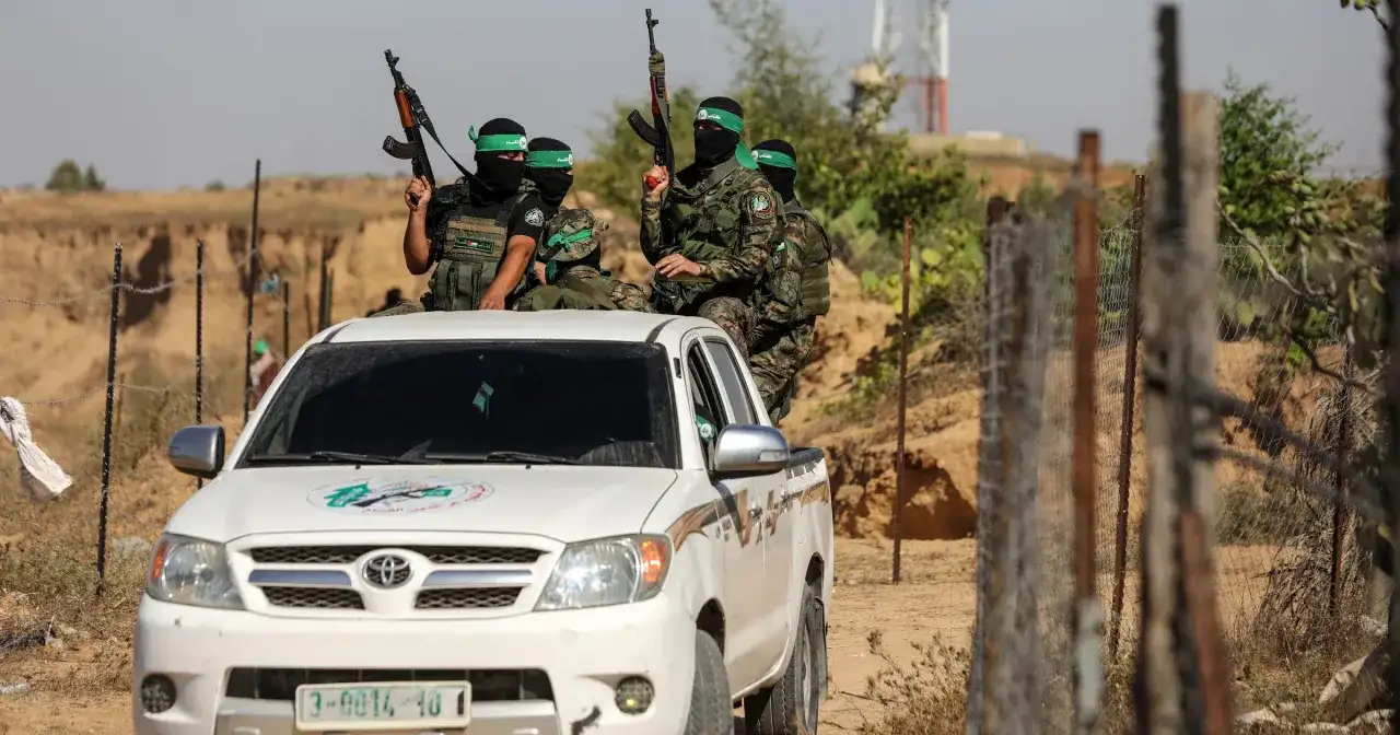 Uzbrojeni bojownicy Hamas w zielonych opaskach na głowach siedzą na białej toyocie, gotowi do akcji.