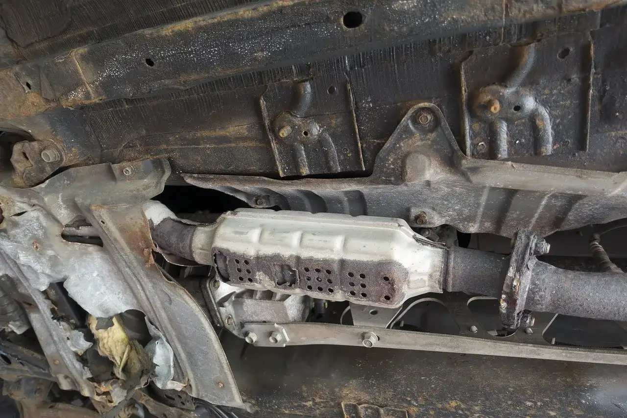 Vue du dessous d'une voiture montrant un catalyseur rouillé, nécessitant un nettoyage catalyseur pour améliorer les performances.
