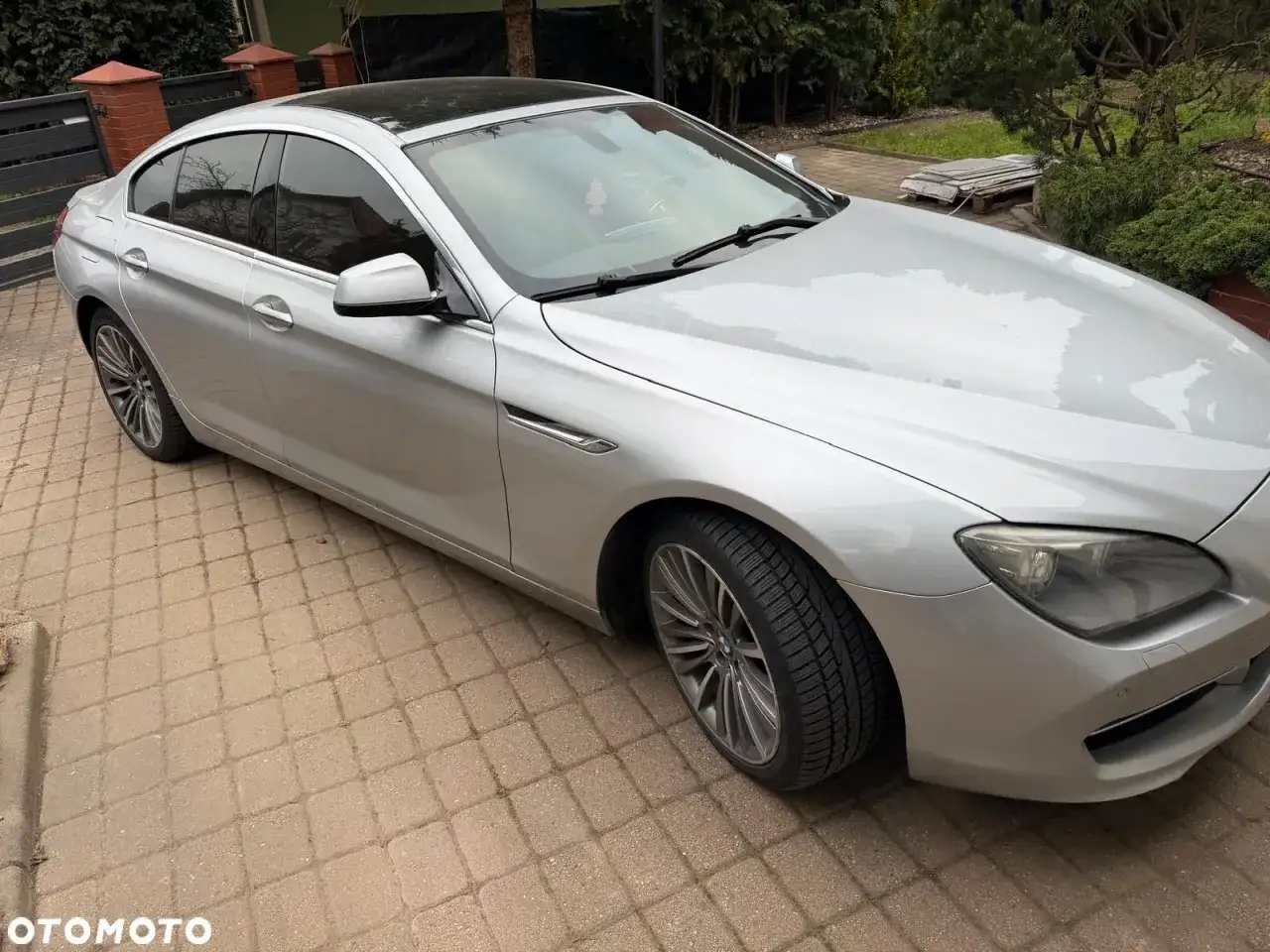 Srebrne BMW 640i z czarnym dachem stoi na podjeździe z kostki brukowej.