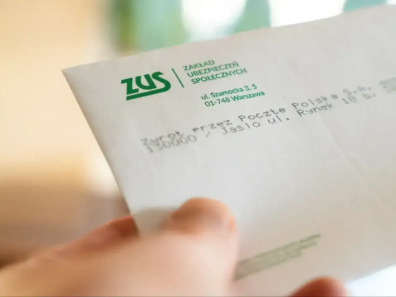 Dłoń trzyma kopertę ZUS. Może to zwrot środków, np. 500 plus dla niepełnosprawnych.