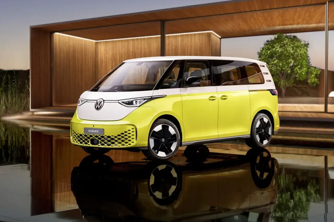 Nowy, elektryczny VW ID. Buzz w dwukolorowym malowaniu, z białym dachem i żółtym nadwoziem, stoi na tle nowoczesnej architektury.