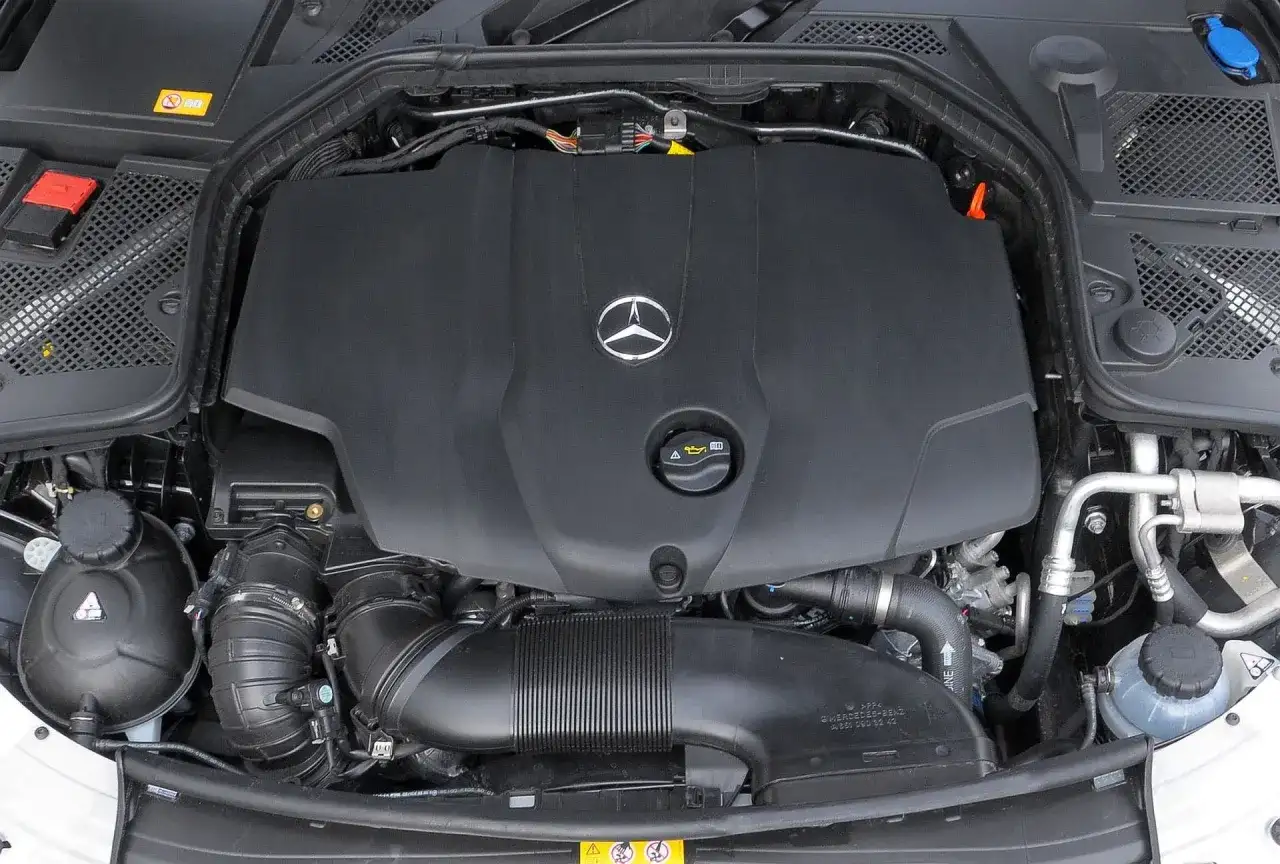 Silnik w Mercedesie C W205. Widoczna czarna osłona z logo producenta, przewody i elementy układu dolotowego.