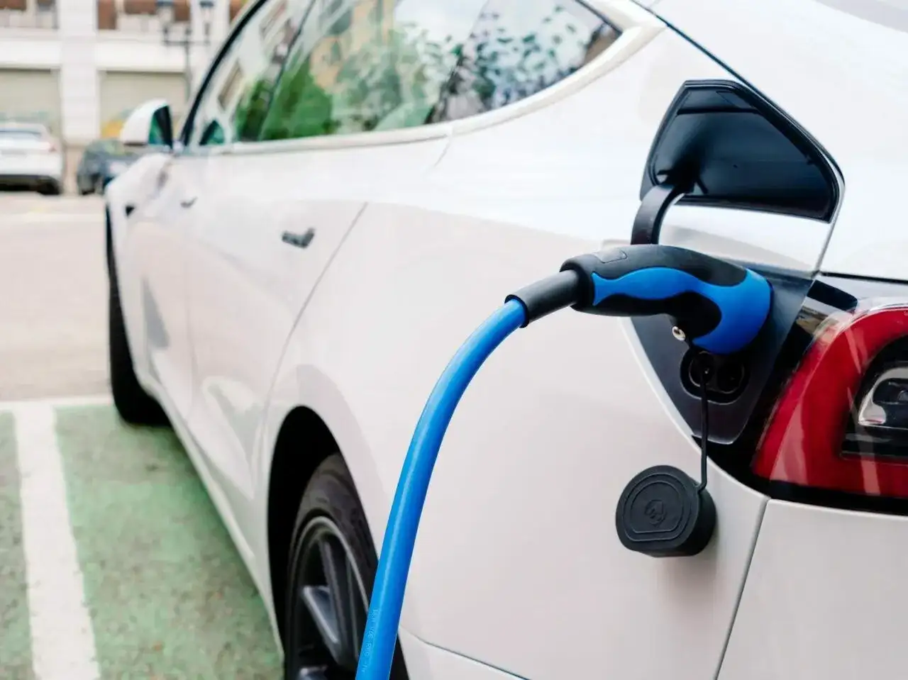 Sekrety doboru opon do aut elektrycznych: dlaczego zwykłe opony niszczą się szybciej? Biały samochód elektryczny podłączony do ładowania.