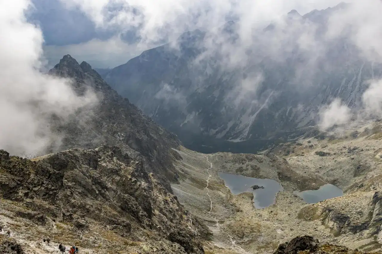 Widok na Tatry Wysokie, z mgłą spowijającą szczyty. Widoczna ścieżka i jeziorka. Planowanie wejścia na Rysy od strony słowackiej i polskiej wymaga dobrej kondycji.