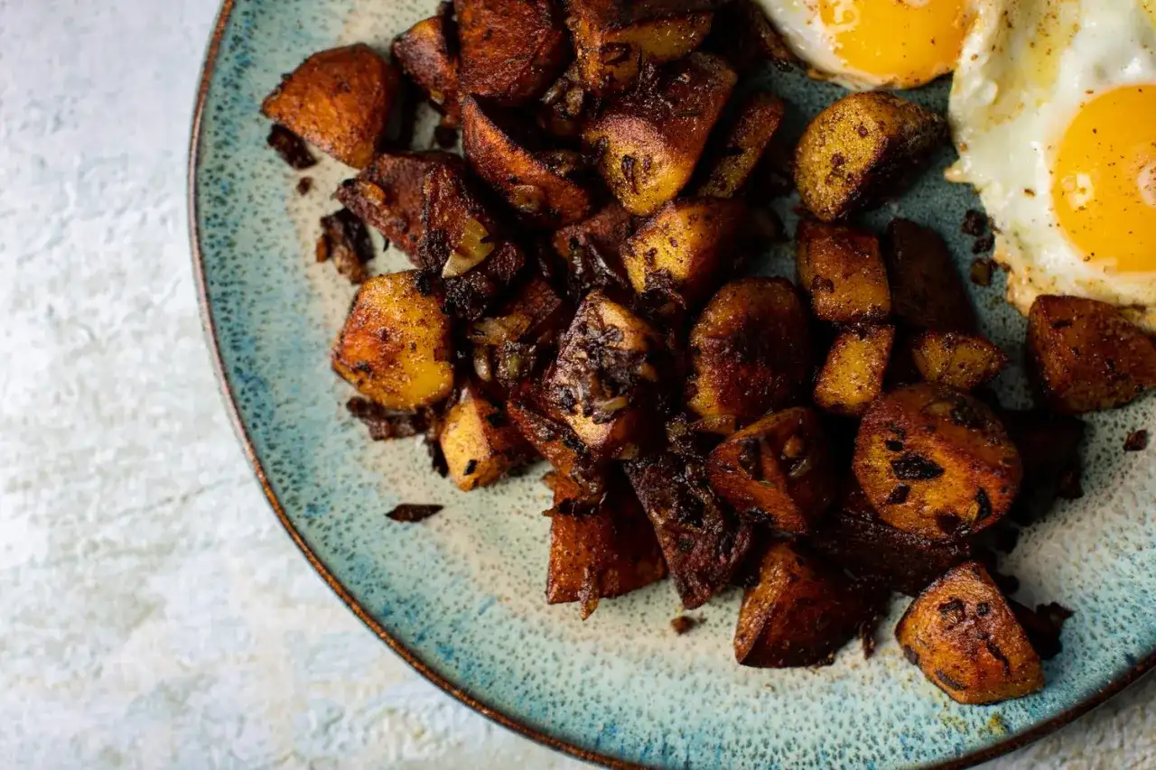 Knusprige bratkartoffeln aus rohen Kartoffeln, goldbraun gebraten, mit zwei Spiegeleiern auf einem rustikalen Teller.