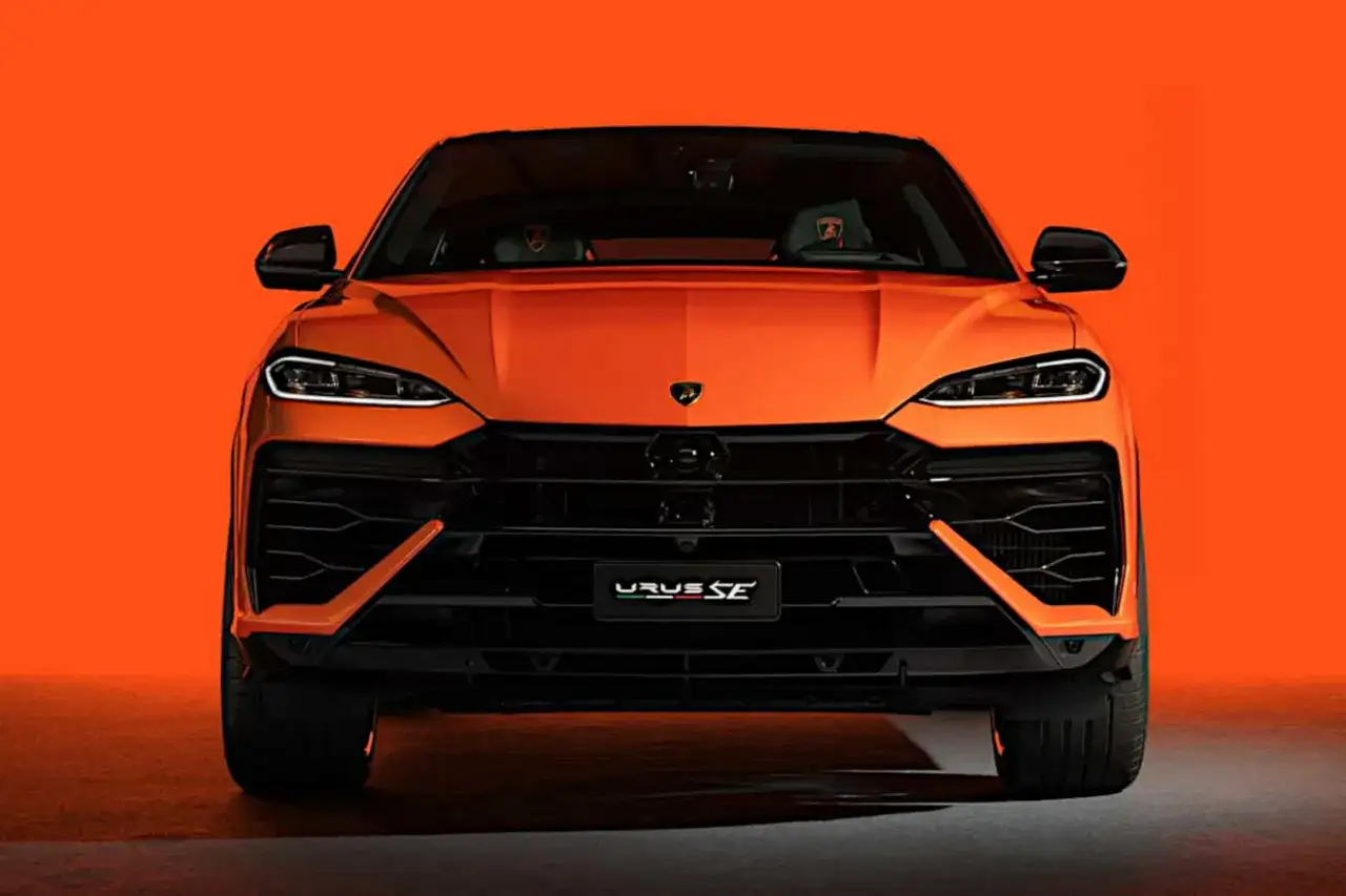 Pomarańczowy Lamborghini Urus SE z przodu, z czarnymi detalami i agresywnym grillem, na tle jaskrawej pomarańczy.