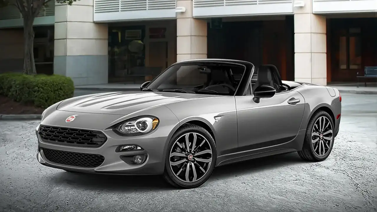 Szary Fiat Spider z czarnym dachem, zaparkowany przed budynkiem.