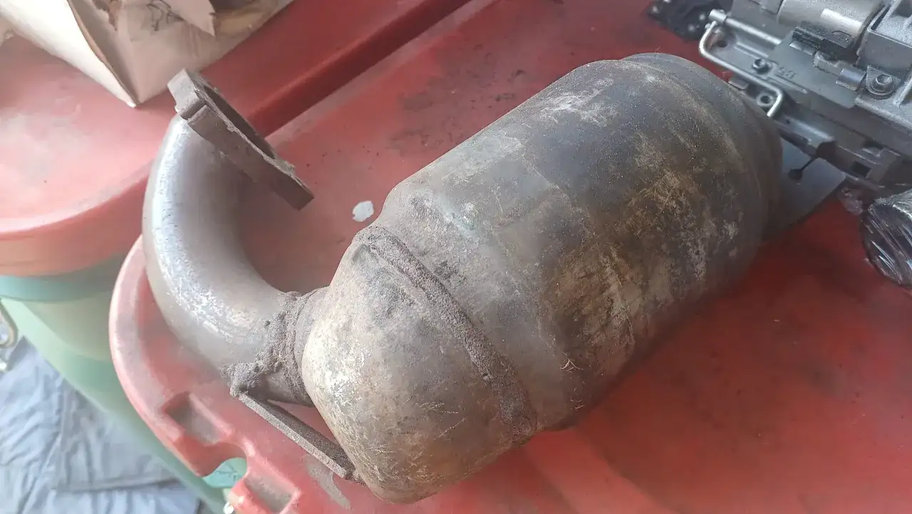 Brudny, skorodowany element układu wydechowego, prawdopodobnie zapchany dpf objawy, leży na czerwonej powierzchni.