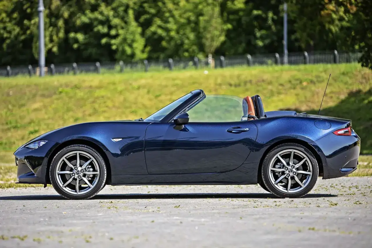Granatowy roadster z otwartym dachem, gotowy na letnią przejażdżkę pośród zieleni.
