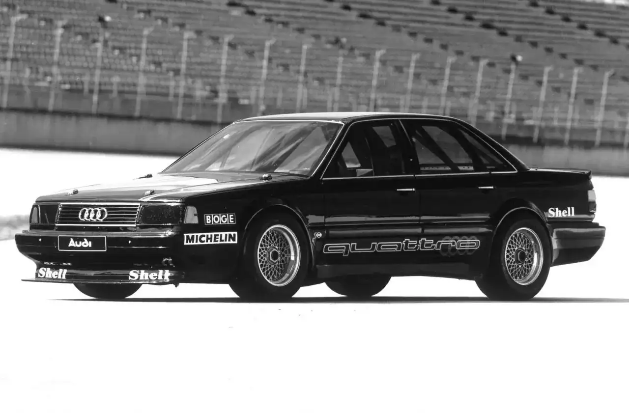 Czarny Audi 5000 Quattro na torze wyścigowym, z logotypami Boge, Michelin i Shell.