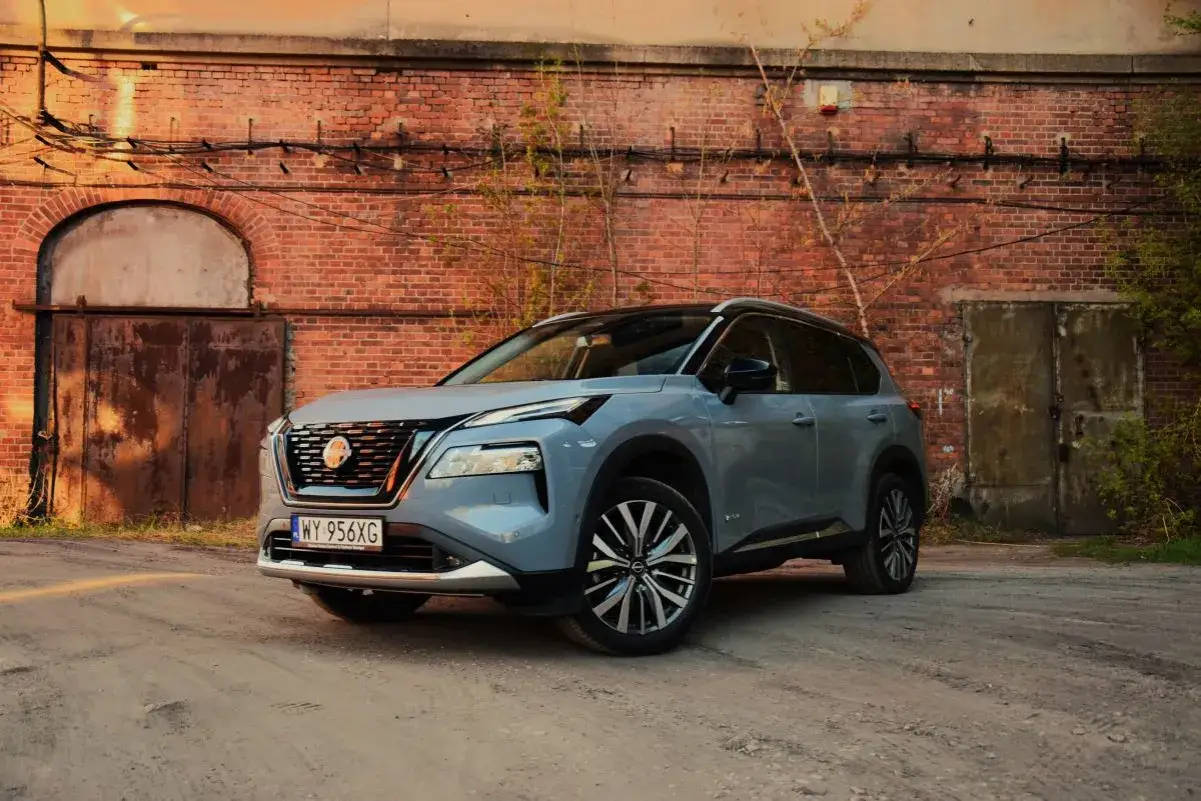 Szary Nissan X-Trail stoi przed starą ceglaną ścianą z zardzewiałymi drzwiami.