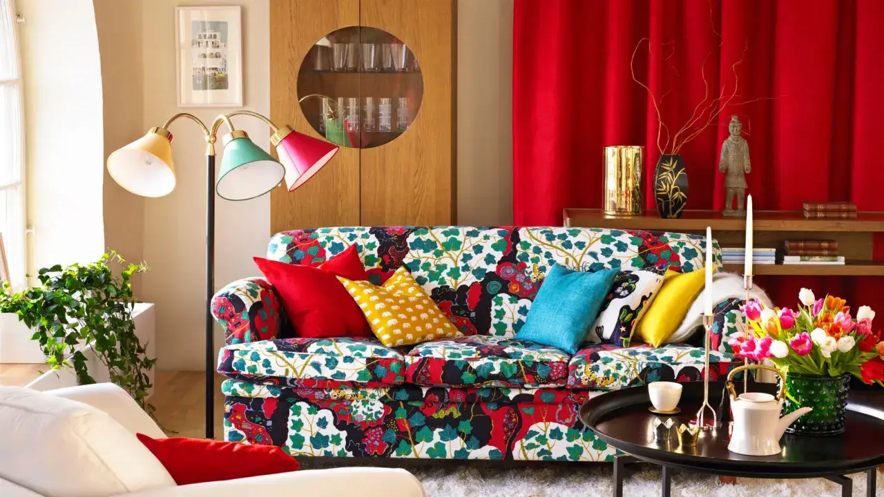 Sofá con estampado floral vibrante, cojines coloridos y una lámpara de pie que evoca un estilo vintage.