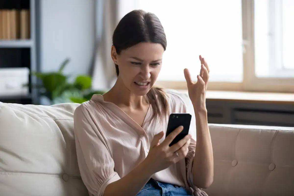 Femme frustrée sur son canapé, regardant son téléphone avec exaspération. Elle dit : "Je ne capte pas chez moi !