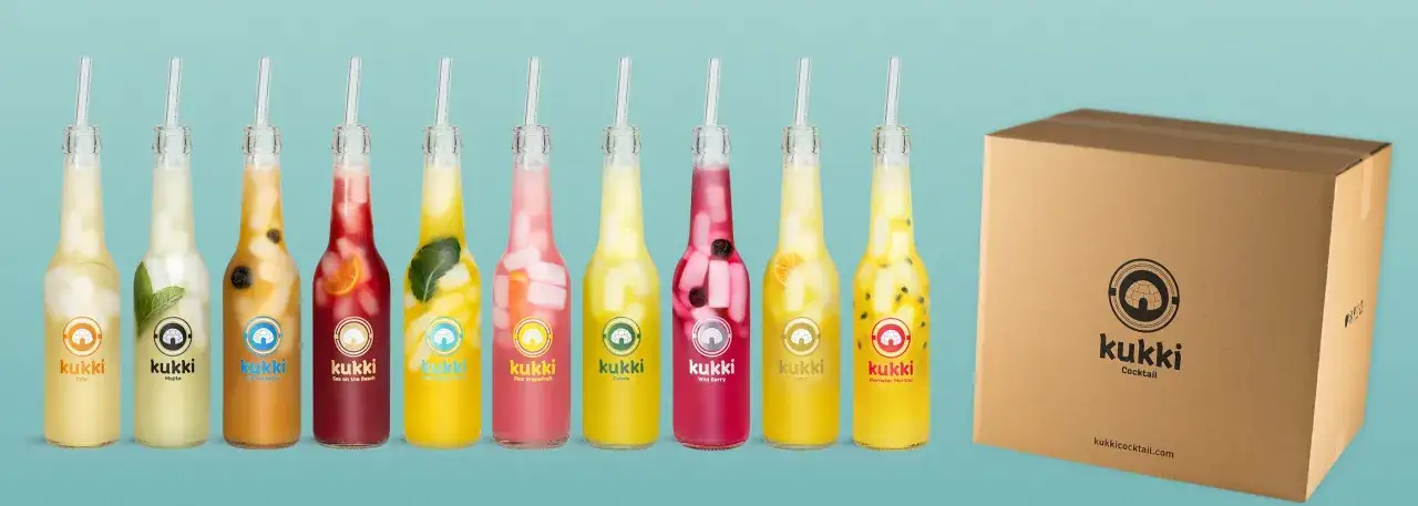 Reihe von Kukki Cocktails in Flaschen mit Früchten und Eis, daneben eine Pappbox.