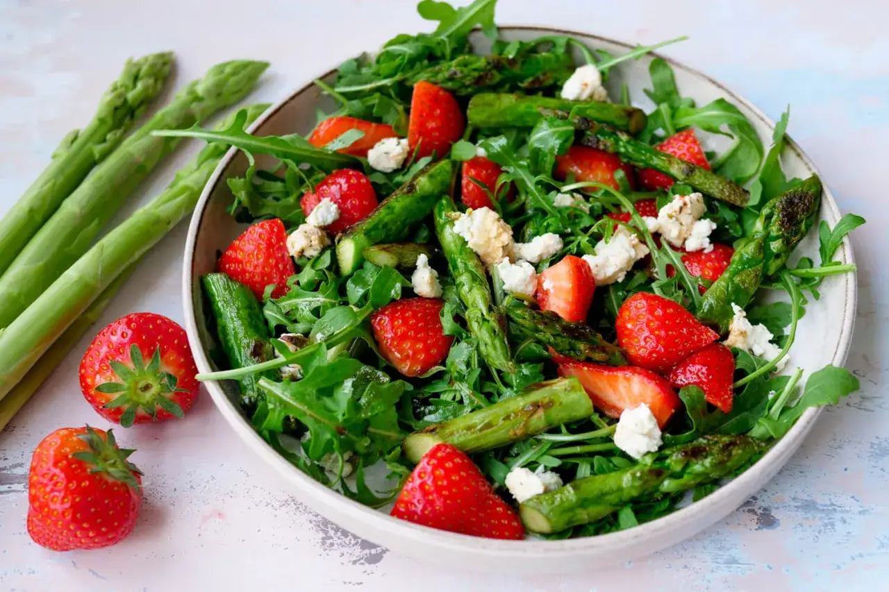 Frischer Spargelsalat mit Erdbeeren und Rucola, garniert mit zerbröseltem Käse.