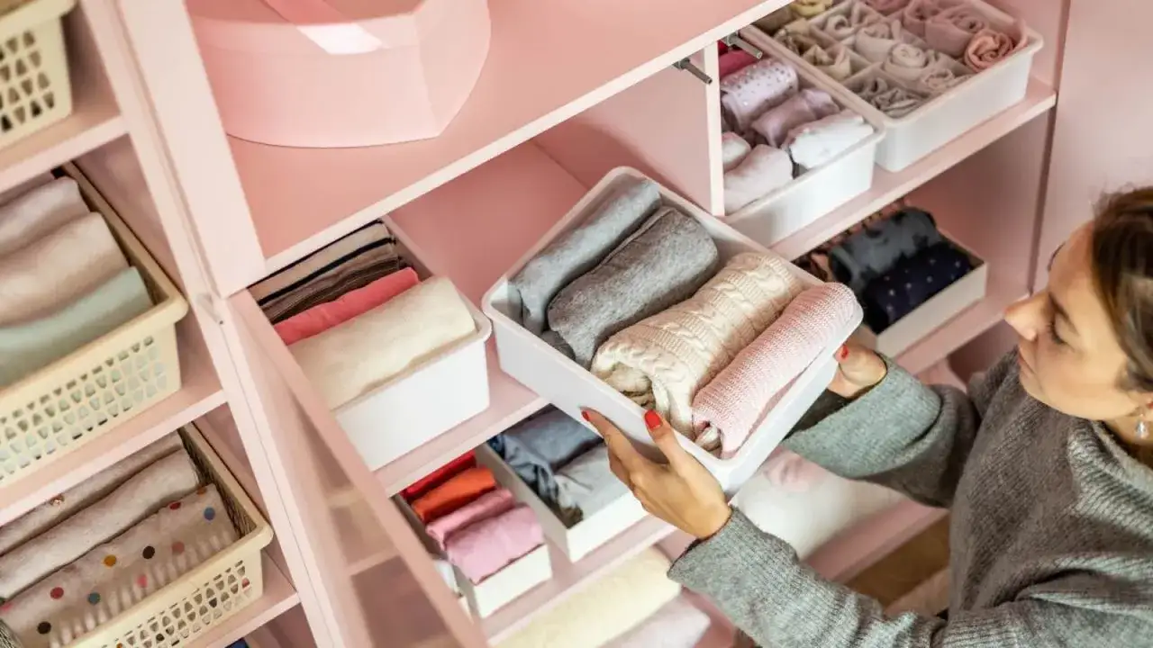 Una mujer organiza su armario, doblando ropa en contenedores. Aprende como ordenar un armario para tener todo a la vista y ordenado.
