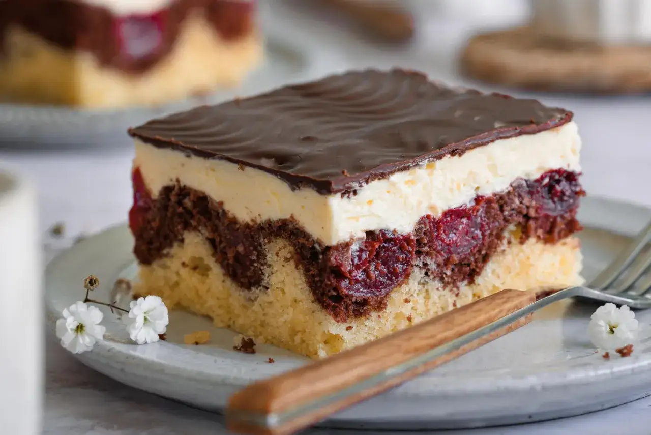 Ein Stück Donauwelle-Kuchen mit Schokoladenglasur, Sahne und Kirschen. Ein köstliches Rezept für den perfekten Genuss.