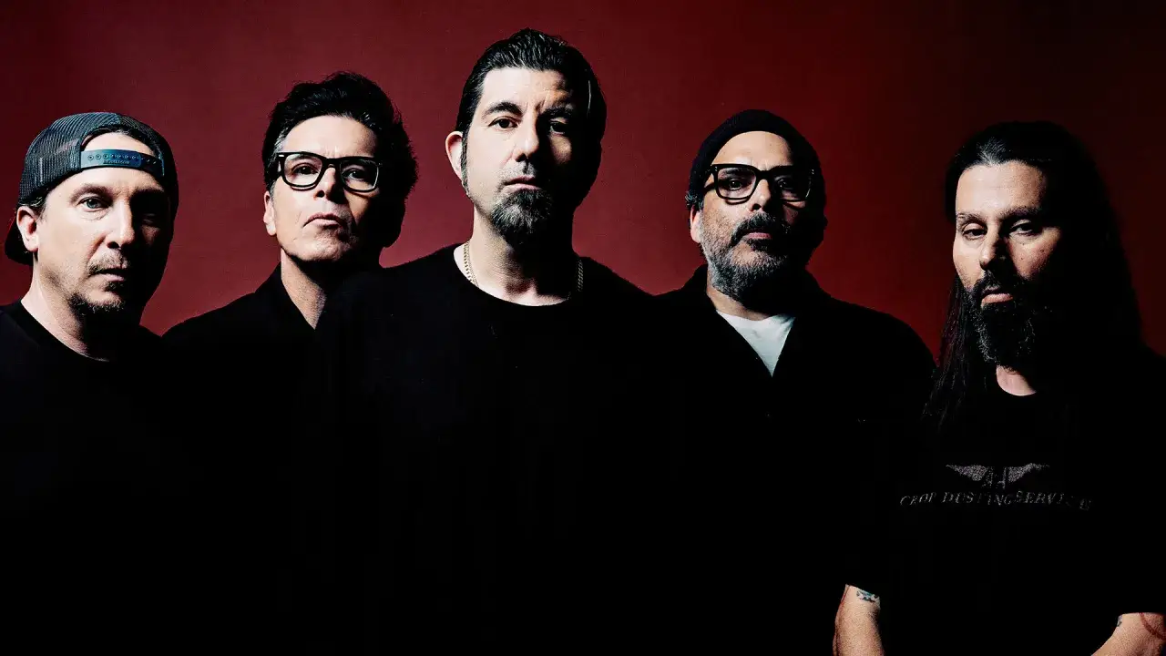 Pięciu mężczyzn, zespół Deftones Polska, pozuje do zdjęcia na ciemnoczerwonym tle.