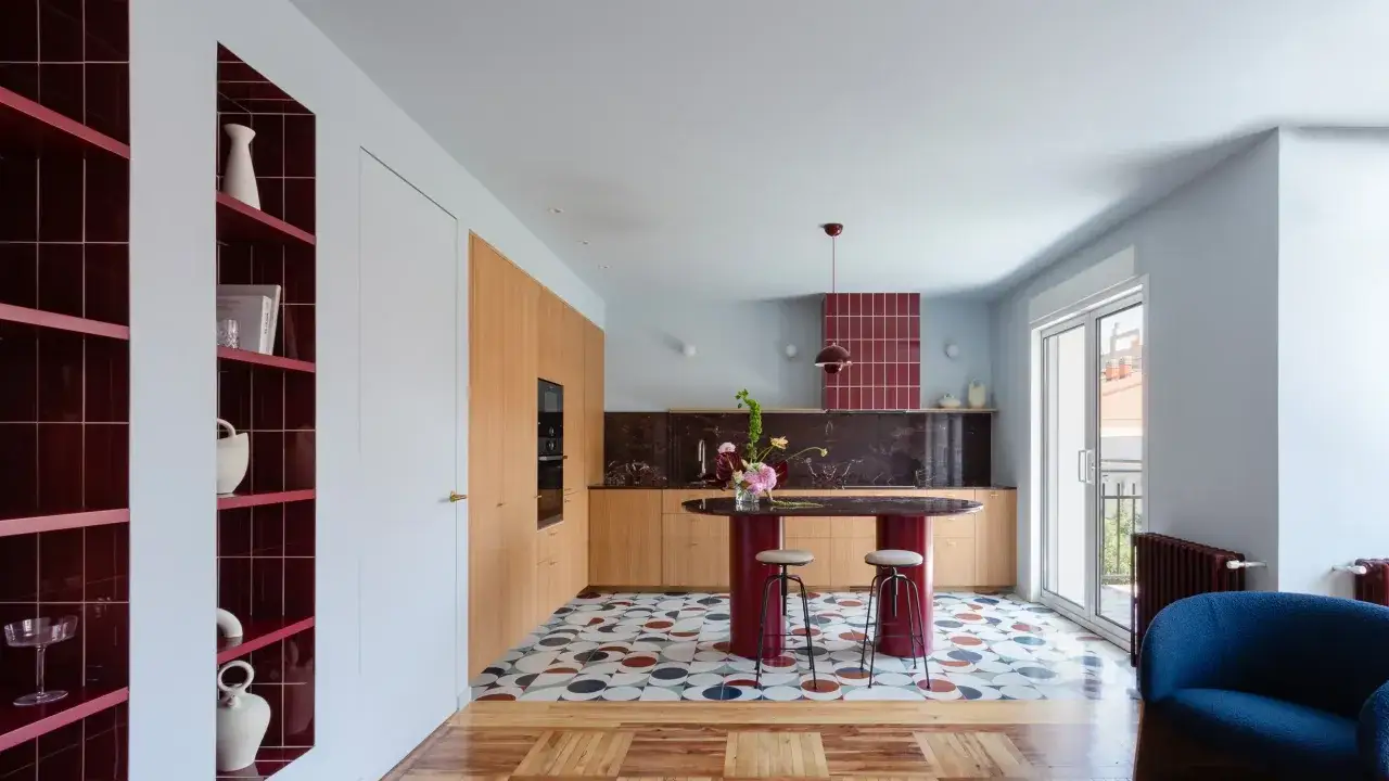 Cocina moderna con isla ovalada, estanterías rojas y suelo geométrico. Un ejemplo de **estudios interiorismo** audaces y coloridos.