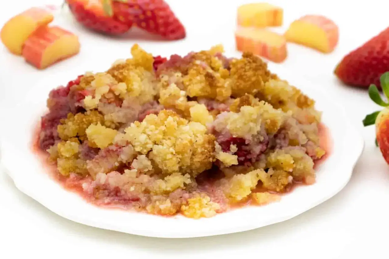 Ein Teller mit warmem Erdbeer-Crumble, garniert mit frischen Erdbeeren und Apfelstücken.