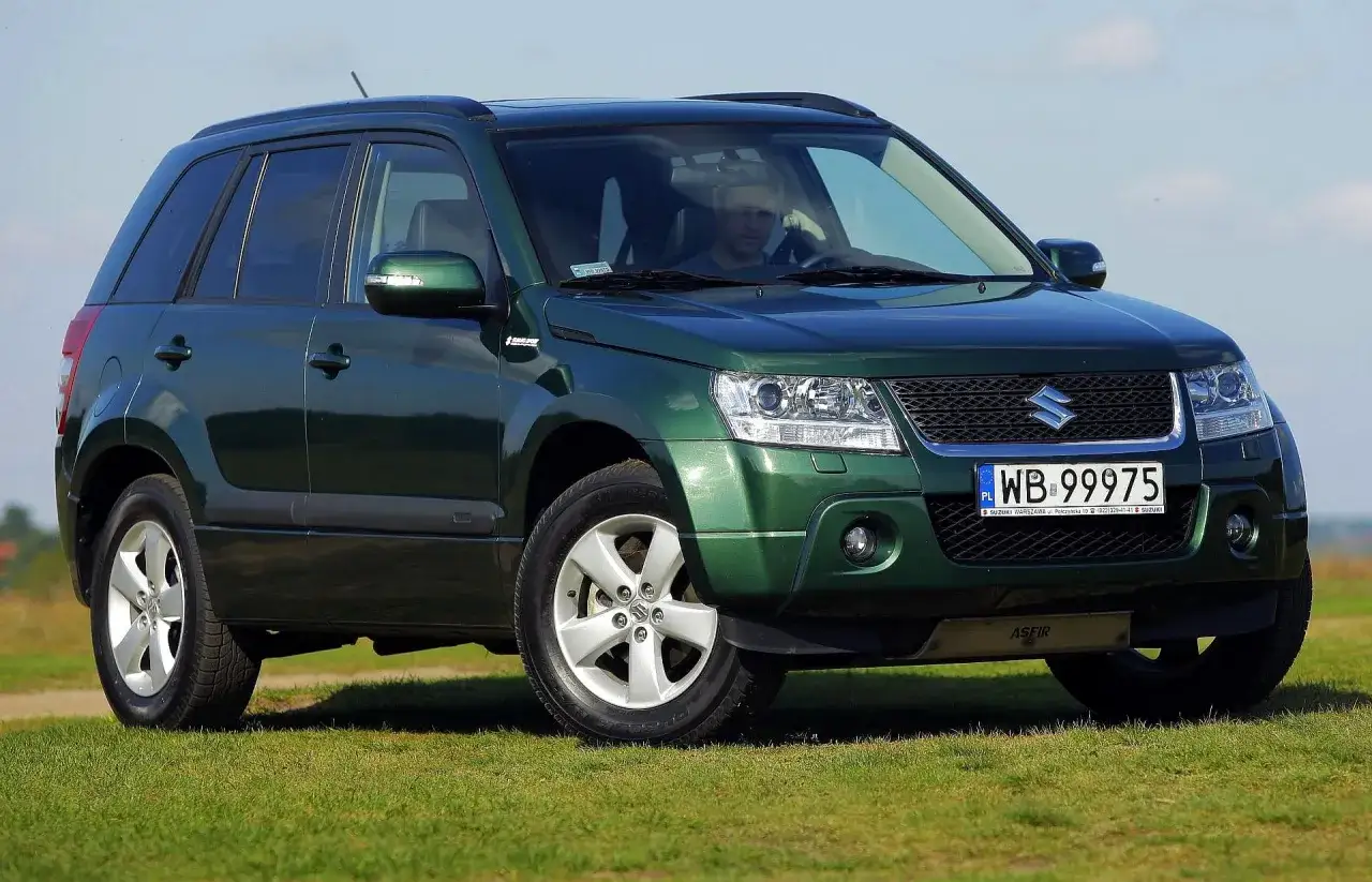Zielony Suzuki Grand Vitara 2 na tle błękitnego nieba i zielonej trawy.