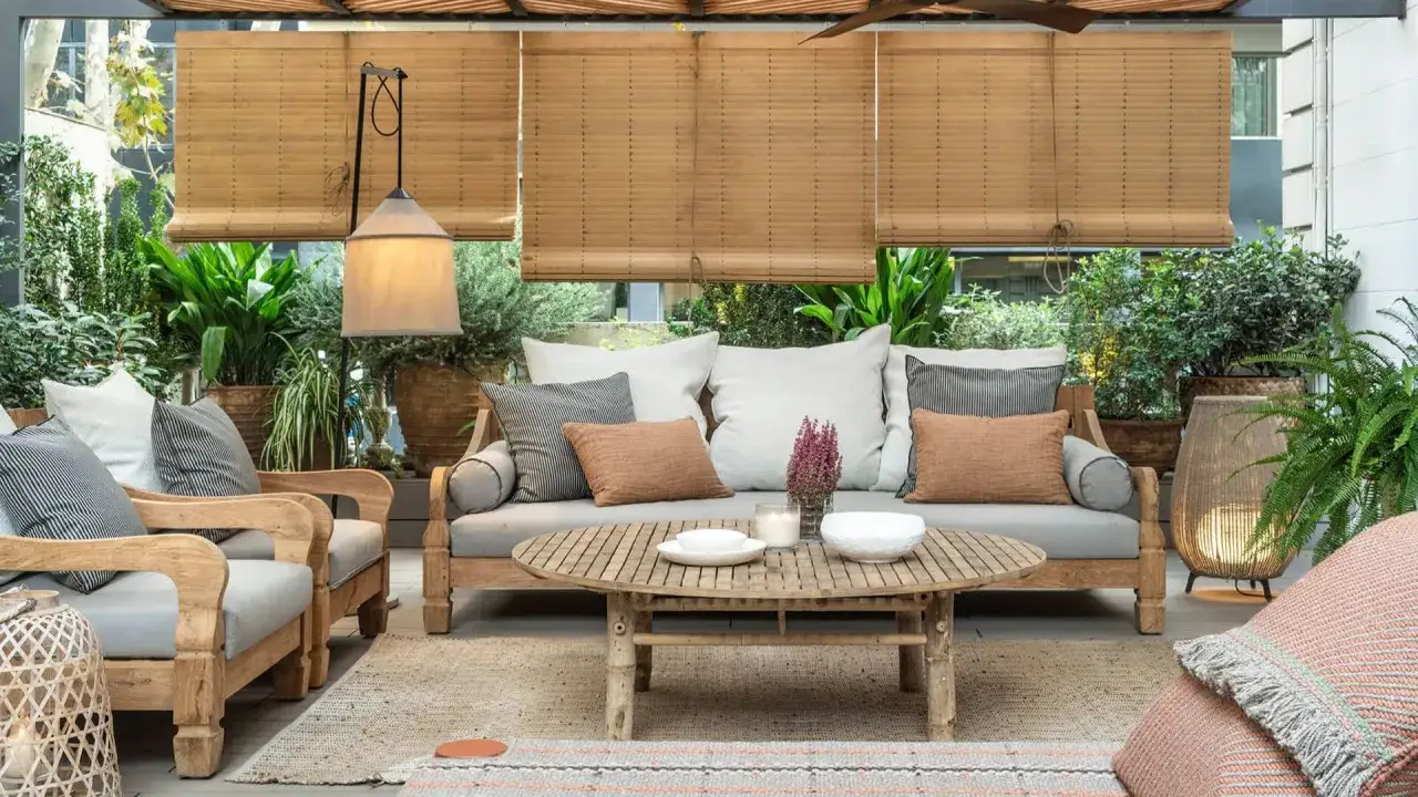 Acogedora terraza estilo mediterráneo con sofá, sillones de madera, mesa de centro y abundante vegetación.