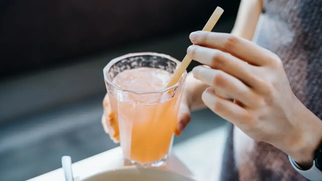 Glas mit rosafarbenem Getränk und Eis, eine Hand hält einen Strohhalm. Vielleicht ein gesunder Drink mit Sauerkrautsaft Inhaltsstoffe.