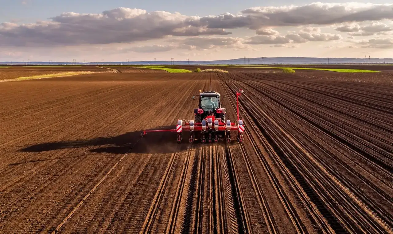 Czerwony traktor z siewnikiem na polu. Zastanawiasz się, ile kosztuje metr ziemi rolnej?