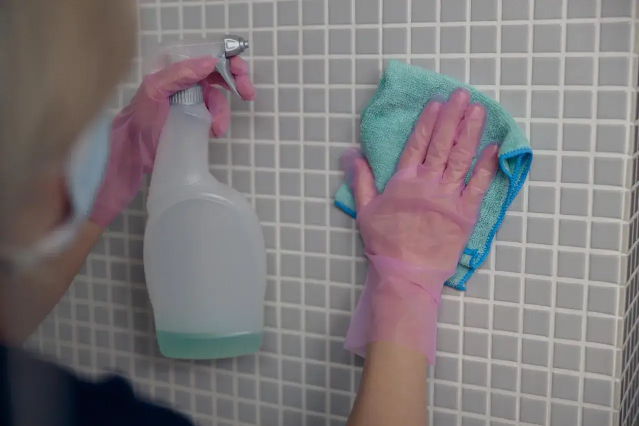 Ręce w różowych rękawiczkach czyszczą płytki. Zastanawiasz się, czym umyć fugi? Spray i ściereczka to dobry początek.