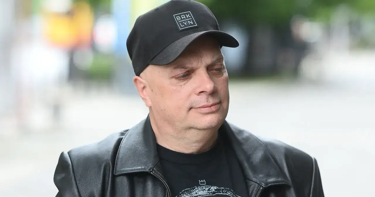 Krzysztof Skiba w czarnej czapce z napisem "BRK LYN" i skórzanej kurtce, zamyślony.