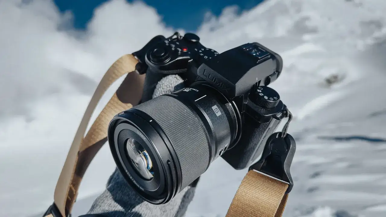 Czarne body aparatu Lumix z obiektywem i beżowym paskiem na tle zaśnieżonych gór.