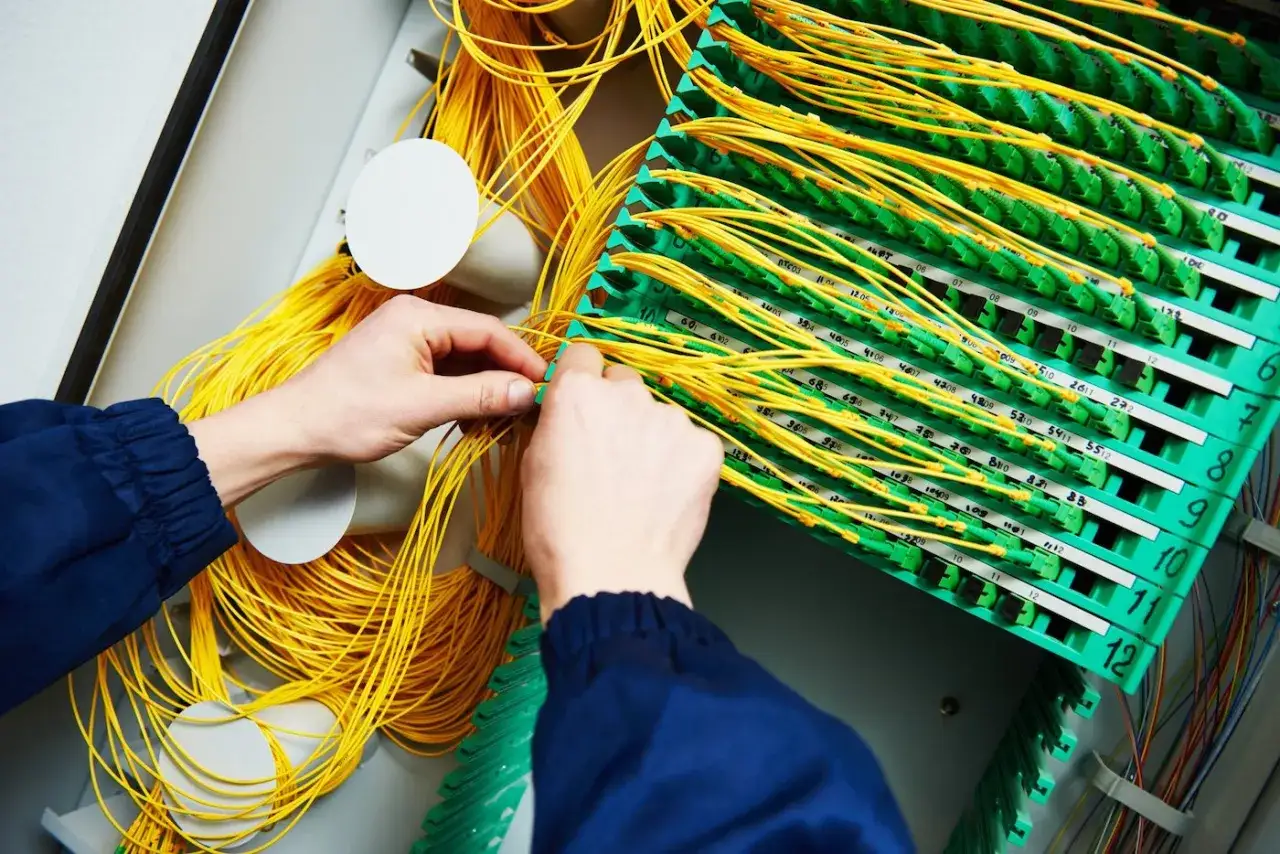 Mains de technicien travaillant sur un panneau de brassage fibre optique, gérant un câble fibre cassé.