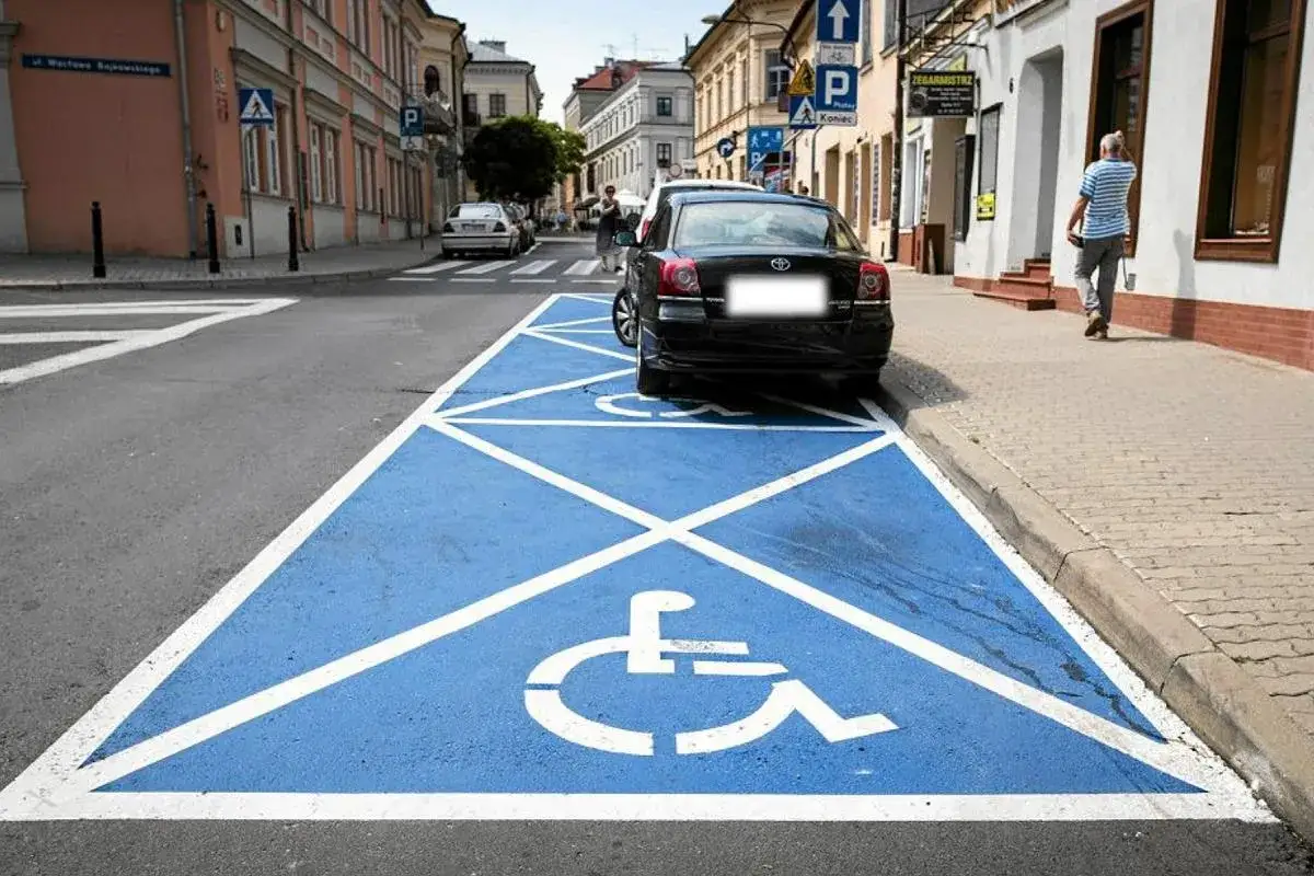 Niebieskie pole parkingowe z symbolem wózka inwalidzkiego. Samochód stoi na miejscu dla niepełnosprawnych, które wymaga karty parkingowej.