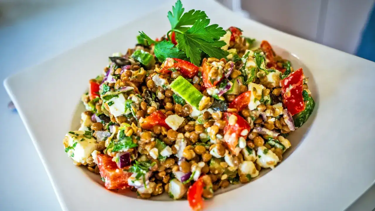 Ein bunter Linsensalat mit Feta, Tomaten, Gurken und frischer Petersilie, garniert mit einem Petersilienblatt.