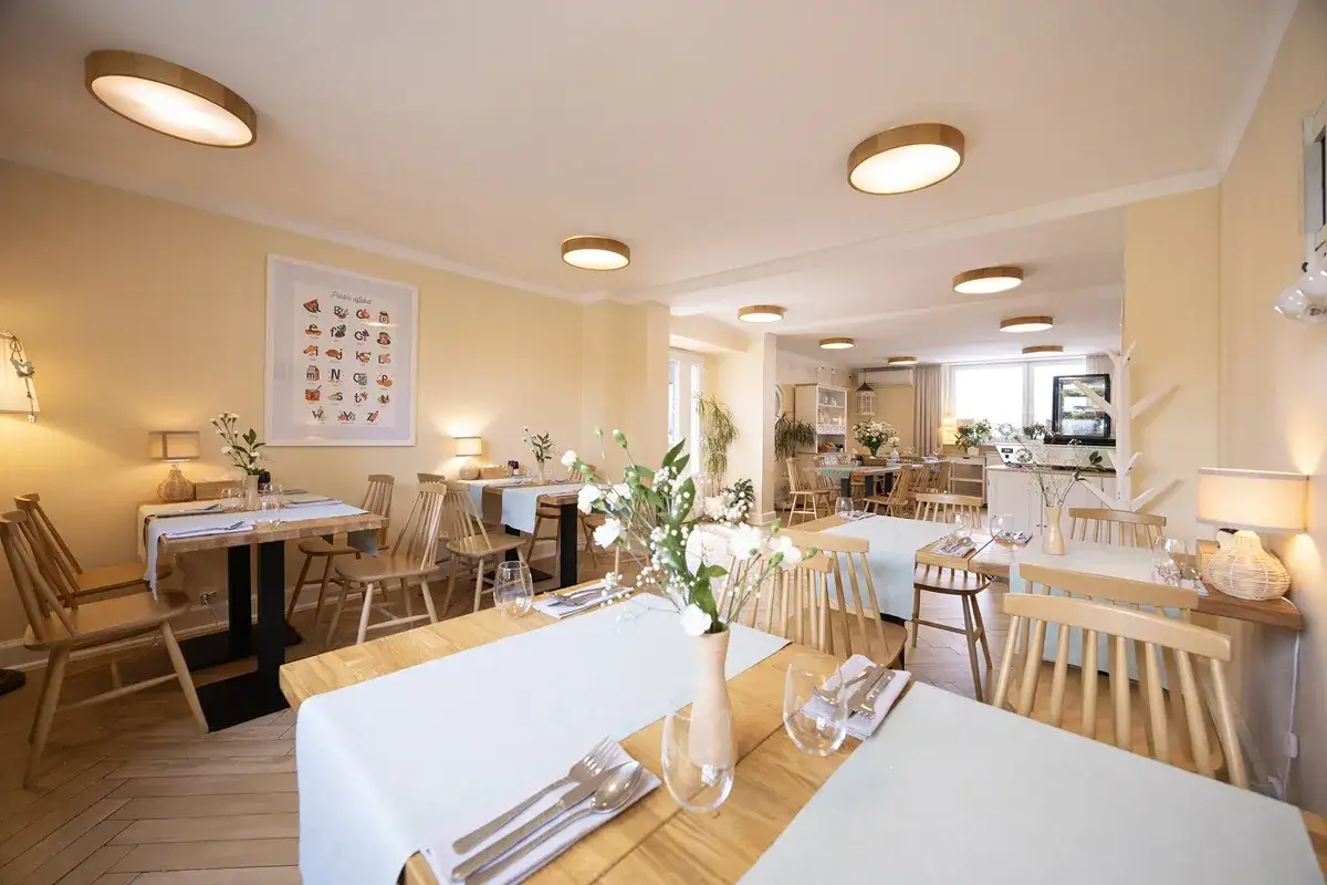 Przytulna restauracja z drewnianymi stołami i krzesłami, idealna na urodziny w łodzi dla dorosłych. Jasne ściany, subtelne oświetlenie i świeże kwiaty tworzą miłą atmosferę.