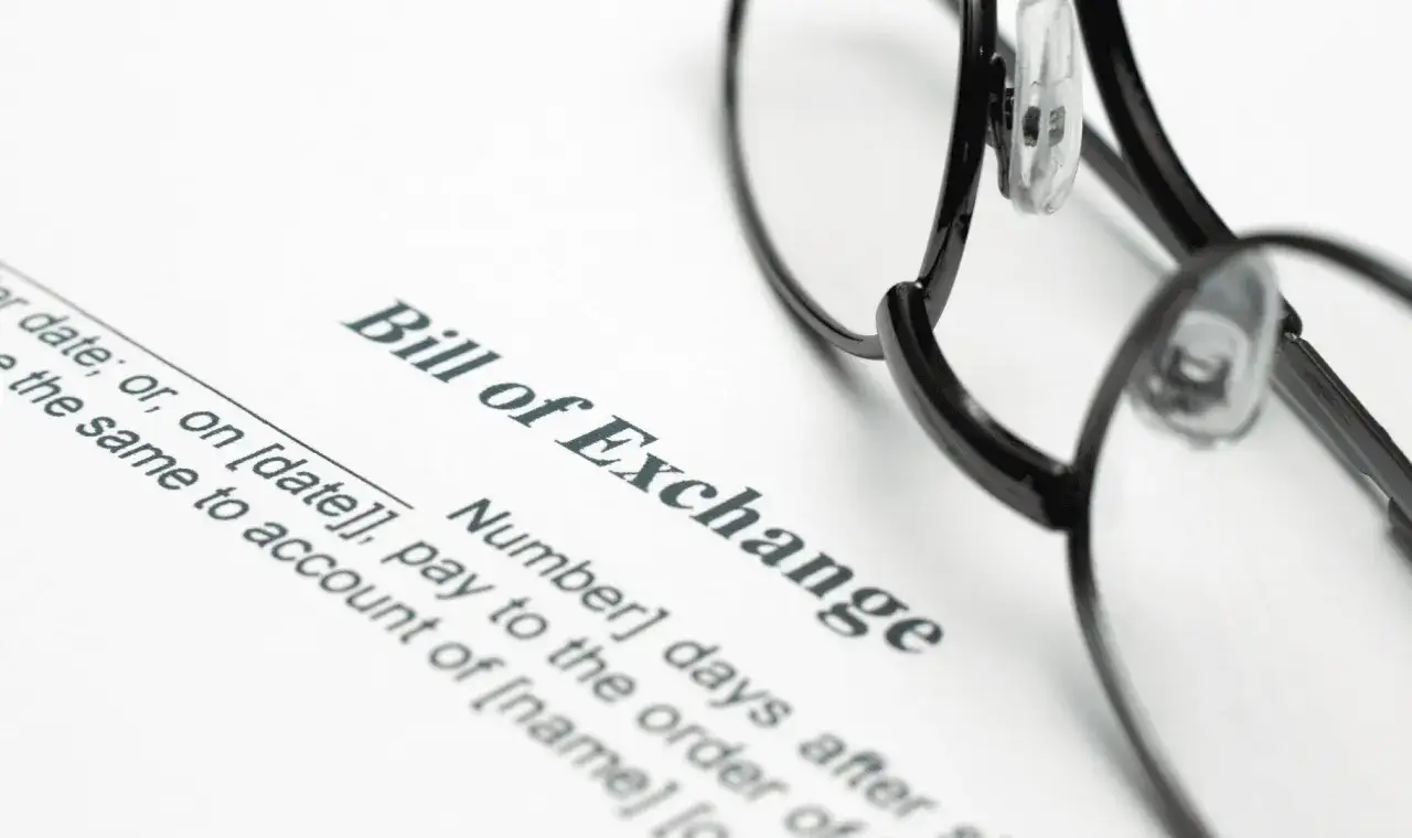 Okulary leżą na dokumencie "Bill of Exchange". To jest weksel, czyli papier wartościowy, który zobowiązuje do zapłaty określonej sumy pieniędzy.