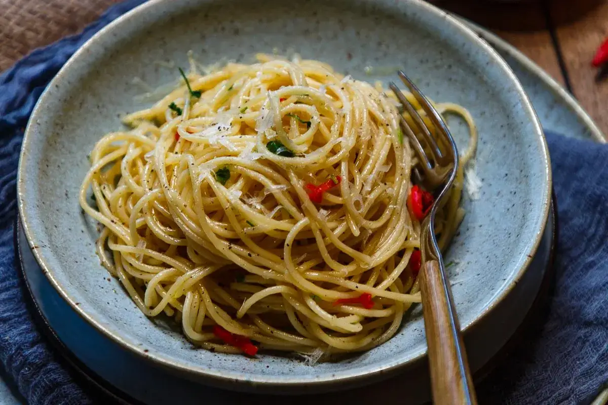 Spaghetti Aglio e Olio mit Chili und Parmesan in einer Schüssel, daneben eine Gabel.