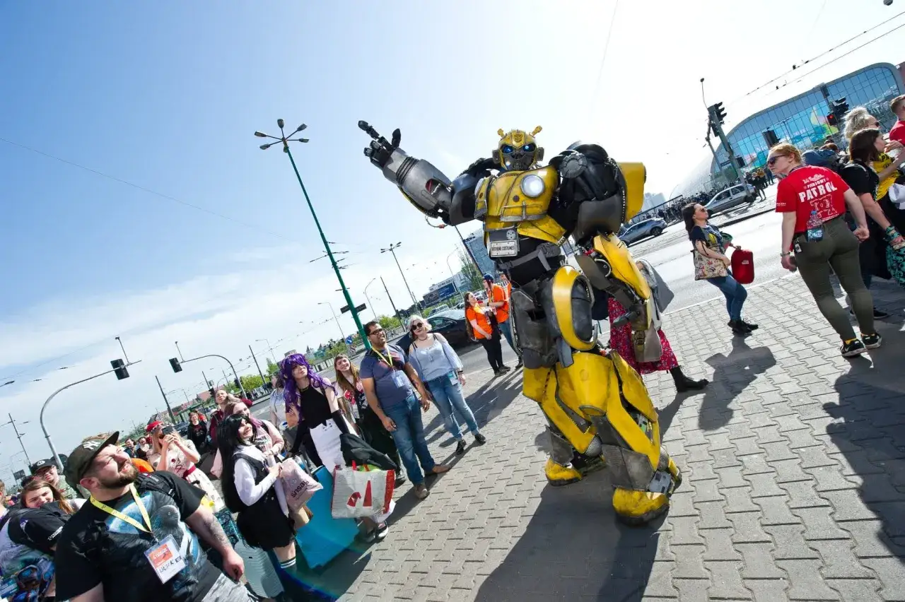 Bumblebee wita fanów na Pyrkonie. Tłum ludzi w kostiumach i z torbami idzie chodnikiem.
