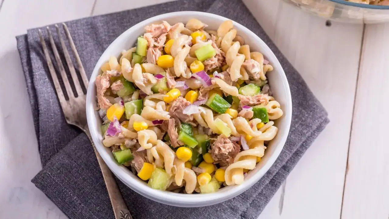 Ein köstlicher nudelsalat mit thunfisch, garniert mit Mais, Gurken und roten Zwiebeln, bereit zum Genießen.