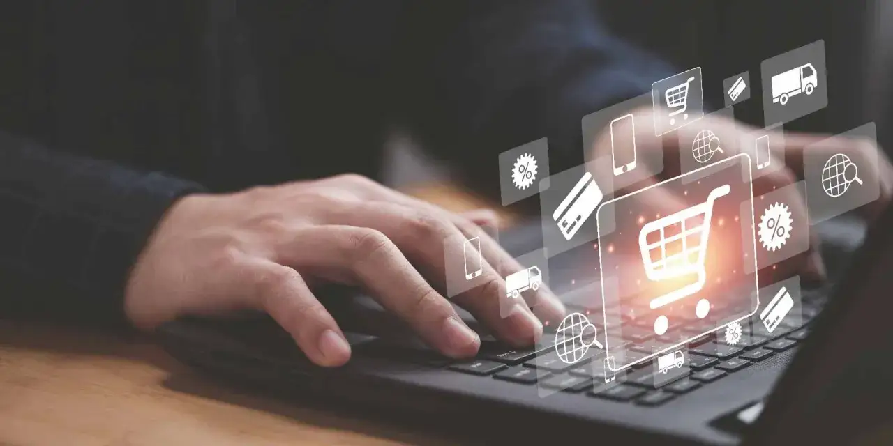 Dłoń na klawiaturze laptopa, nad nią ikony symbolizujące e-commerce: koszyk, karta płatnicza, ciężarówka, procenty, globus.