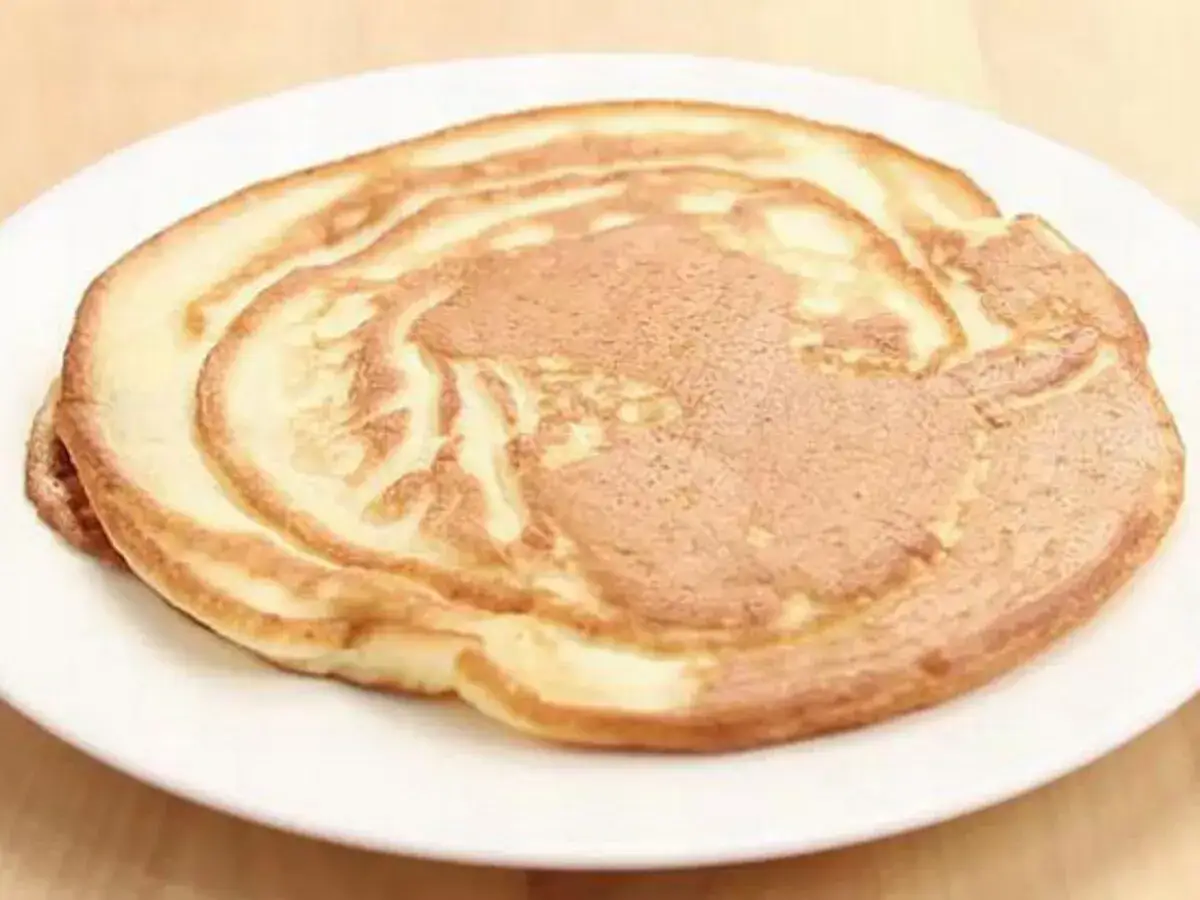 Ein goldbrauner Pfannkuchen ohne Ei auf einem weißen Teller, perfekt für ein leichtes Frühstück.
