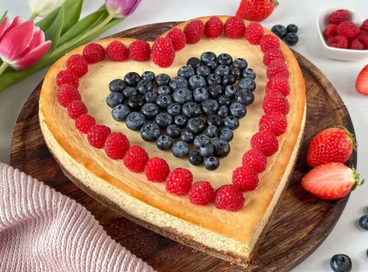 Herzförmiger Kuchen zum Muttertag, dekoriert mit Himbeeren und Blaubeeren. Ein süßes Dankeschön für Mama.