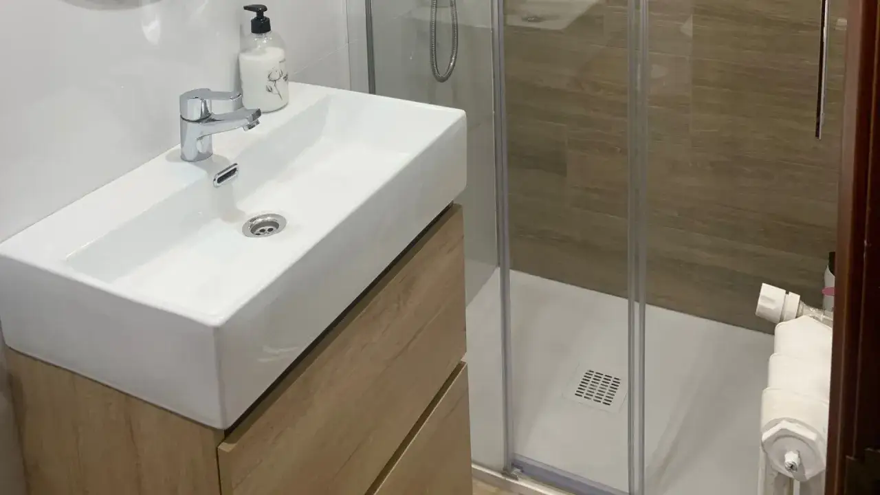 Moderno lavabo sobre mueble de madera, ducha con mampara y azulejos imitación madera. ¡Renovar baño sin obra es posible!