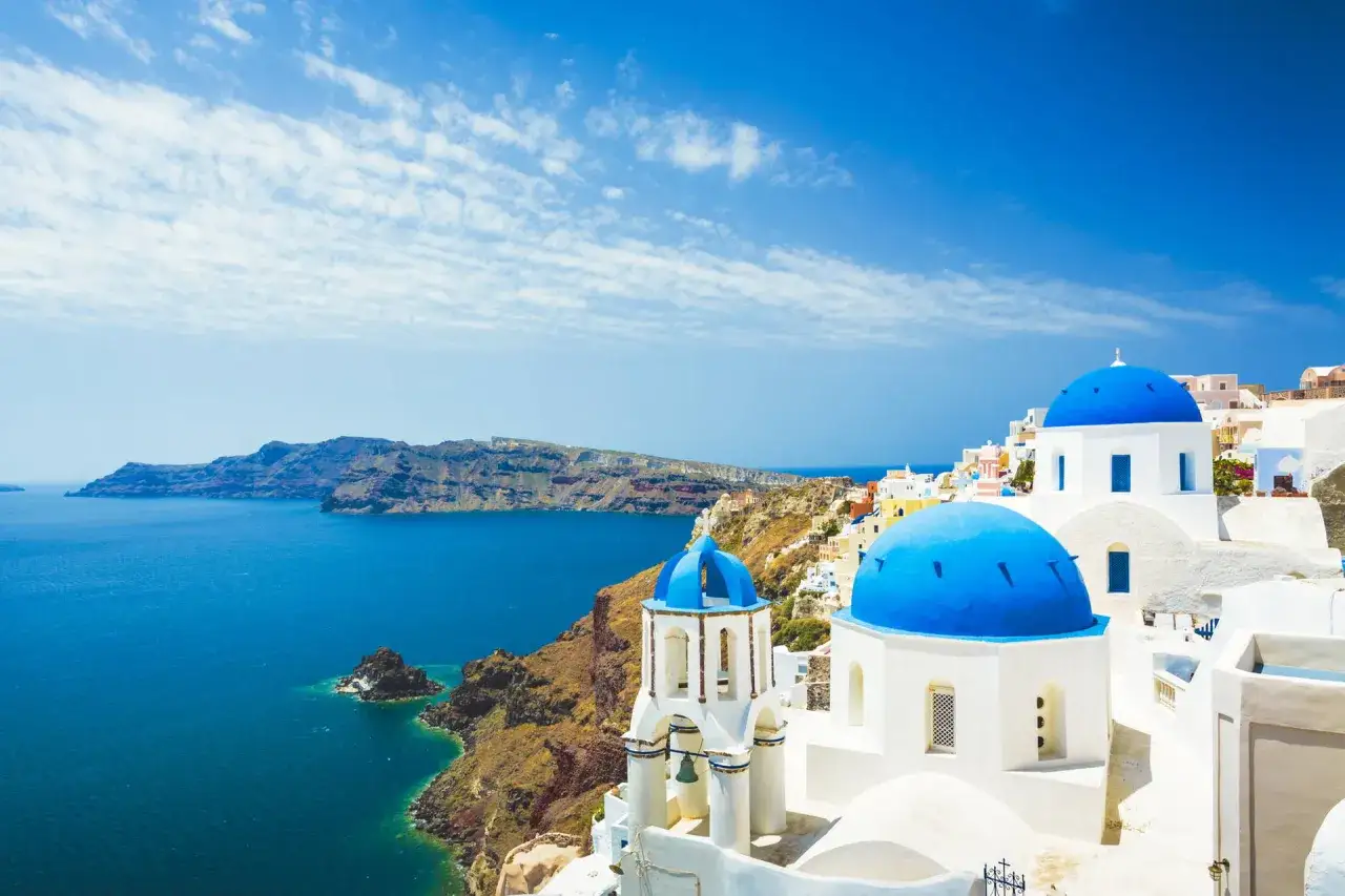 Santorini: białe domy, niebieskie kopuły kościołów i turkusowe morze. Idealne miejsce na tanie wakacje w Grecji.