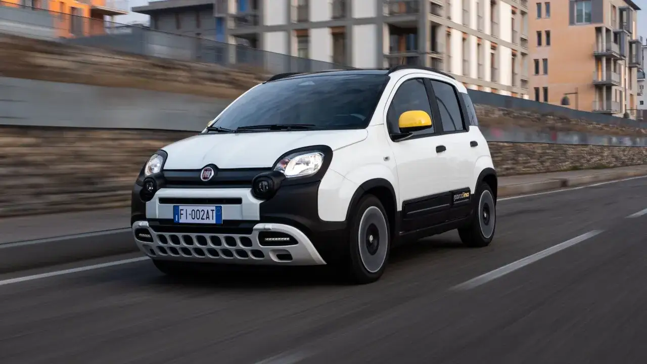 Biały Fiat Panda 3 z żółtym lusterkiem jedzie po drodze.
