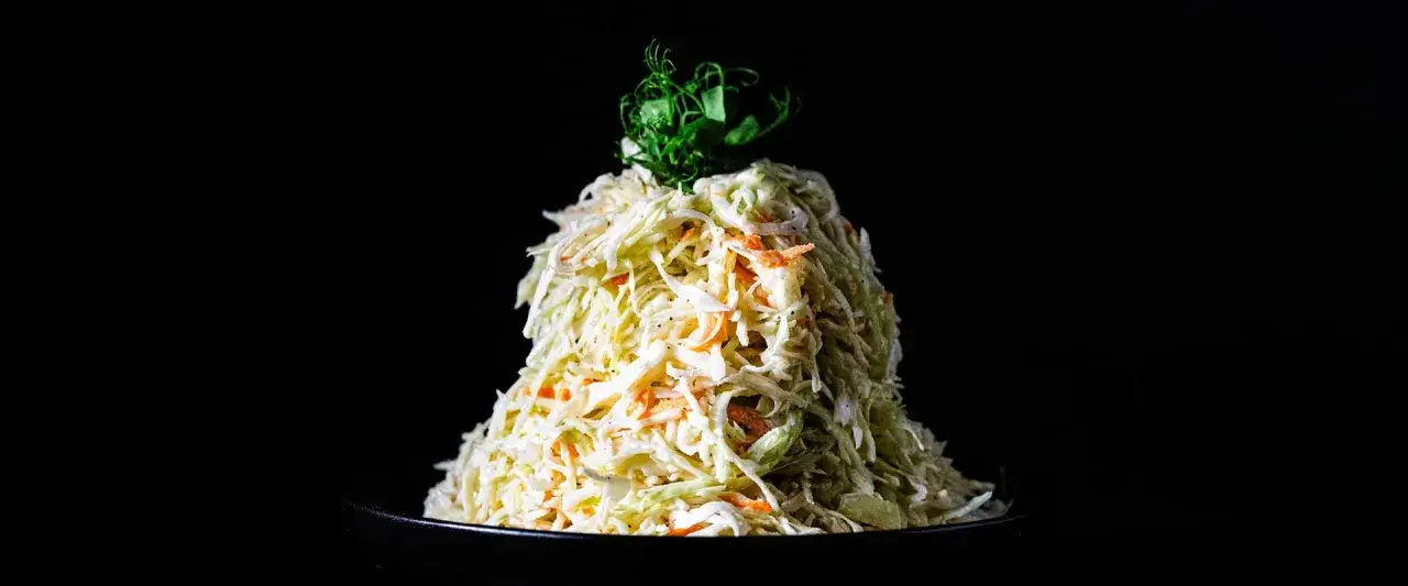 Ein Berg aus Krautsalat mit Karotten, verfeinert mit cremigem coleslaw dressing, gekrönt von grünen Sprossen.