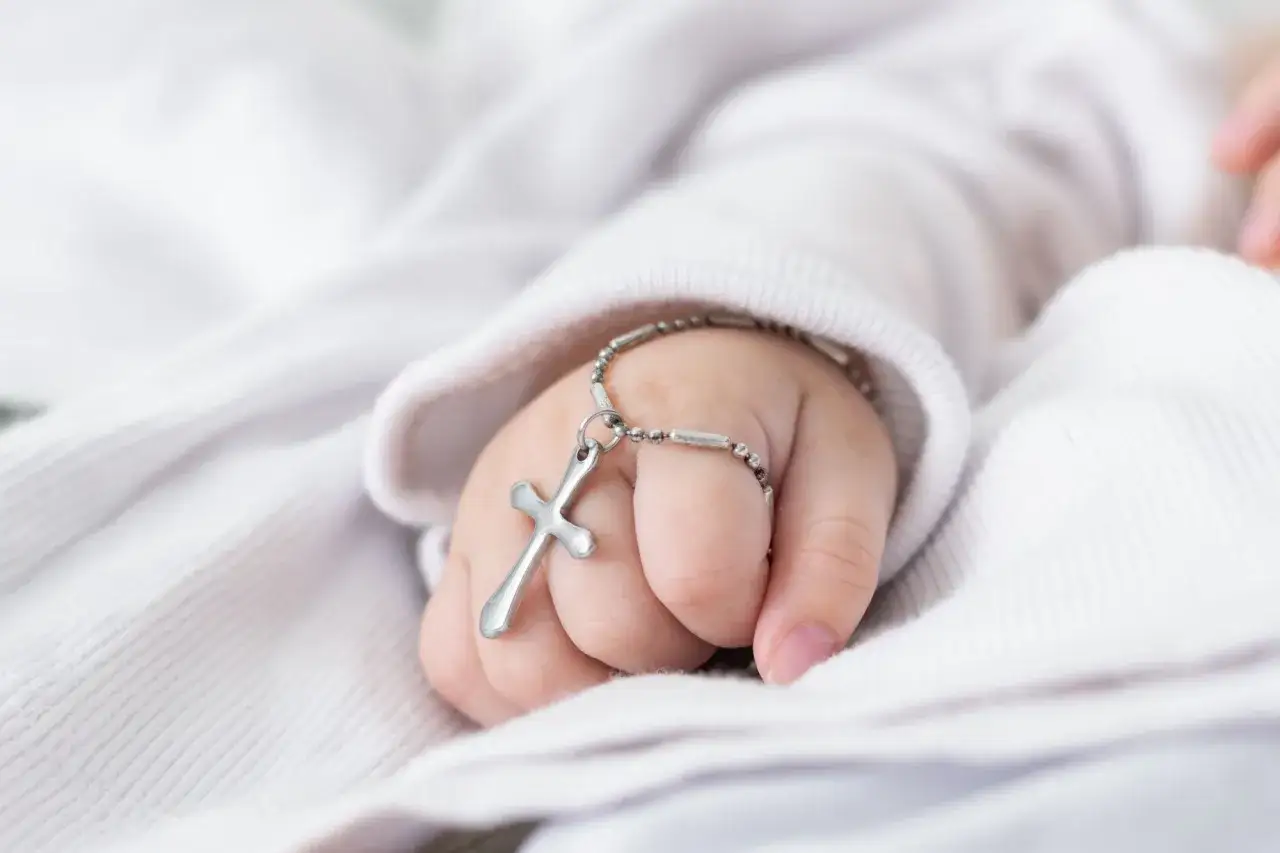 Dziecięca rączka z krzyżykiem na łańcuszku. Chrzestny na chrzciny często daje taki symboliczny prezent.