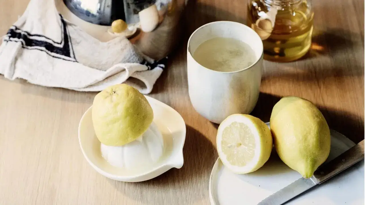 Zitronentee bei Halsschmerzen: frische Zitronen, ein Glas Tee und Honig auf einem Holztisch.